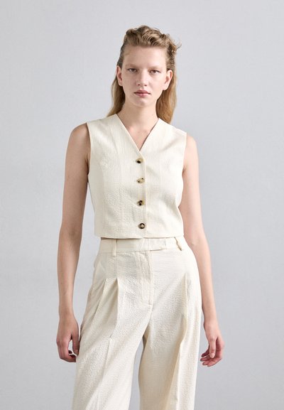White textured sleeveless top with a v-neck and three decorative buttons, paired with matching high-waisted, pleated wide-leg trousers.