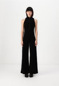 Black jumpsuit with a high collar, full zipper front, wide-legged trousers, and a soft texture. Features minimalistic design and no visible patterns.