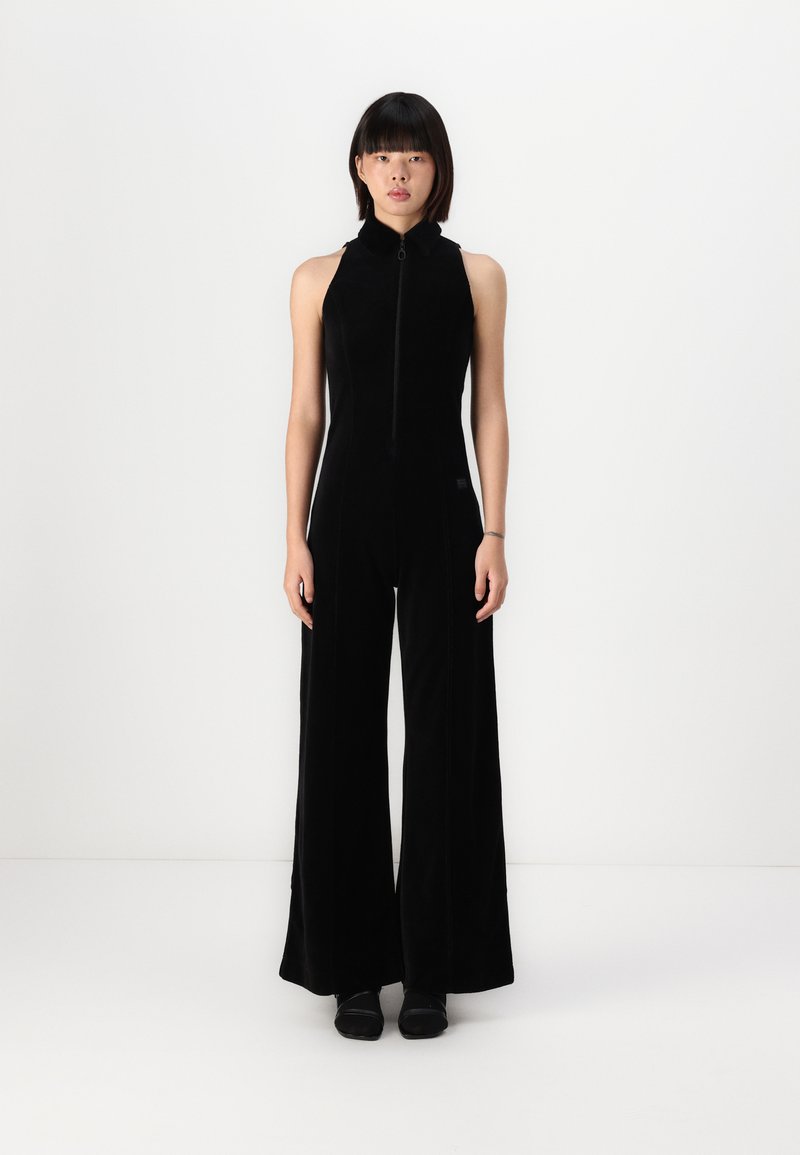 Black jumpsuit with a high collar, full zipper front, wide-legged trousers, and a soft texture. Features minimalistic design and no visible patterns.