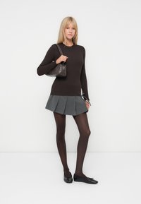 Maglione a maniche lunghe marrone in maglia con colletto a cuore, gonna plissettata grigia, collant scuri e ballerine nere. Tiene una piccola borsa scura.
