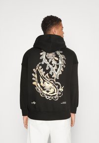 Felpa nera con maniche lunghe e un grande motivo paisley sulla schiena, con dettagli metallici in argento e oro. Materiale in cotone morbido.