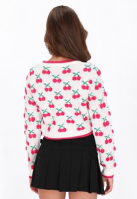 Biely pletený sveter s vzorom ružových čerešní, zelenými listami a červeným rebrovaným výstrihom. Nosí sa s čiernou plisovanou sukňou.