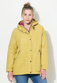 Gul vattentät jacka med huva, med tryckknappar, dragkedjefickor och kontrasterande innerfoder. Slät, lättviktsmaterial.