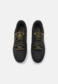 Zapatillas negras deportivas con texturas de malla y ante, cordones en color verde olivo y suela blanca. Presenta un logo en el lateral y costuras en contraste.