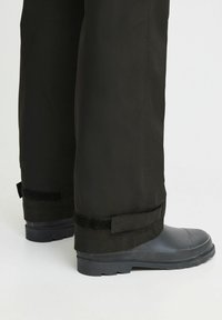 Black waterproof pants with adjustable Velcro cuffs, paired with gray rubber boots featuring a textured sole and sturdy design.