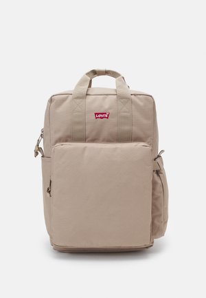 Mochila de tela beige con dobles asas superiores, bolsillo frontal con cremallera y bolsillo de malla lateral. Cuenta con un logo rojo de Levi's en la parte frontal.