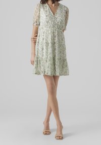 Robe fleurie en tissu vert pâle avec un décolleté en V, des manches courtes bouffantes et une jupe à volants. Présente un imprimé floral délicat sur toute la surface.