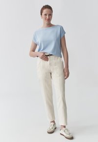Svetle modrý krátký rukáv top spárovaný se smetanovými úzkými kalhotami. Outfit obsahuje černý pás a světlé tenisky s béžovým akcentem.