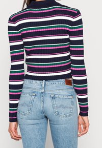 Ribbstickad tröja med horisontella ränder i marinblått, vitt, grönt och rosa; åtsittande design; tillsammans med ljusblå högmidjade jeans.