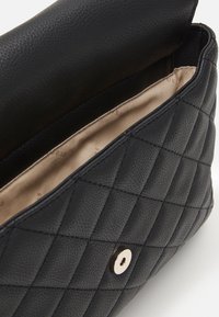 Sac à main en cuir noir matelassé avec une finition texturée, doté d'une fermeture à pression dorée et d'une doublure en tissu beige à l'intérieur.