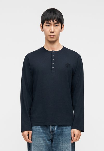 Μπλε σκούρο πουκάμισο με μακρύ μανίκι, λαιμόκοψη henley με πέντε κουμπιά, μαλακό ύφασμα, διακριτικό κεντημένο λογότυπο στο στήθος και άνετη γραμμή.