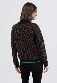 Sweter w panterkę z brązową bazą i czarnymi plamami, z czarnym prążkowanym kołnierzem i mankietami z zielonymi akcentami.