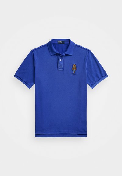 Zils polo krekls, kas izgatavots no kokvilnas. Iezīmē divu pogu apdari, īsas piedurknes un izsistīts logo kreisajā krūtī. Gluda tekstūra.