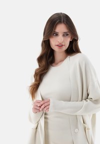 Hellbeige Cardigan mit lockerer Passform, geripptem Textur und einer einzelnen Knopfverschlussschließe, über einem passenden gerippten Rundhalsausschnitt-Shirt getragen.