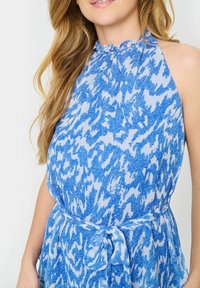 Modrá halter top s vlnitým vzorem, s volánovým výstřihem a zavazovacími pasem. Lehká, poloprůhledná tkanina vytváří splývavý design.