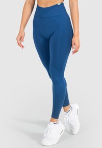 Blaue hochtaillierte Leggings, dehnbare Stoffe, glatte Textur, taillierter Schnitt, kombiniert mit weißen Sneakers, die kontrastierende Farben zur Schau stellen.