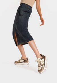 Gonna midi in denim con spacco frontale, abbinata a sneakers metalliche oro e beige con dettagli testurizzati e una suola bianca spessa.