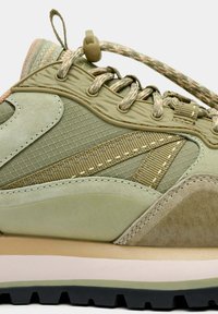 Zapato de senderismo verde que combina materiales de ante y malla, diseño redondeado, paneles texturizados y una entresuela beige contrastante.