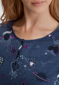 Navyblaues T-Shirt mit kurzen Ärmeln, das ein Muster aus Sternen und Herzen zeigt, mit einem runden Ausschnitt und einer Knopfleiste mit zwei Knöpfen auf der Brust. Weicher, strukturierter Stoff.