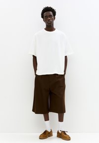 Hvid oversized t-shirt, brune knælange shorts, brune sko og hvide sokker. Glat tekstur, afslappet pasform og minimalistisk design.