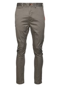 Pantaloni slim-fit in cotone verde tenue. Presentano una chiusura con bottone, tasche frontali e una texture sottile. Una tasca ha un accento rosso.