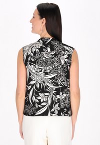 Top negru fără mâneci, cu un model floral alb, textură moale și decolteu rotund, cu un croi ușor larg și tiv.