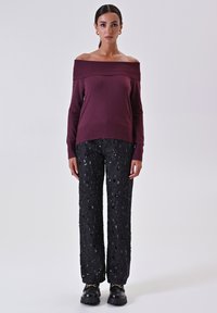 Burgunderfarbener Off-Shoulder-Pullover kombiniert mit schwarzen, mit Pailletten besetzten Hosen. Weit geschnittenes Design, strukturierter Stoff und klobiges schwarzes Schuhwerk.