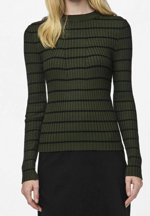 Femme portant un pull ajusté à manches longues, côtelé, vert foncé avec des rayures horizontales noires et une jupe noire.