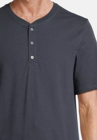 Man som bär en mörkgrå kortärmad henley-tröja med tre knappar och V-hals. 