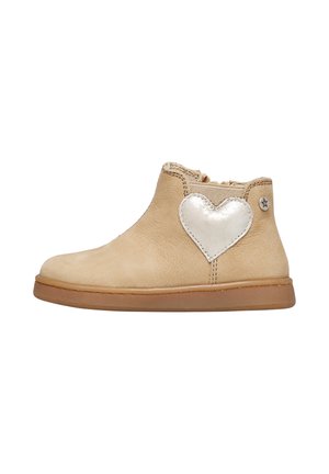 Stivaletto in pelle beige con una patch a forma di cuore metallico argento sul lato, dotato di una suola in gomma flessibile e un colletto imbottito.