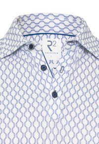 Korte mouwen met kraag in het wit met een blauw geometrisch patroon. Bevat twee donkere knopen en een label met R2 Amsterdam, maat L.