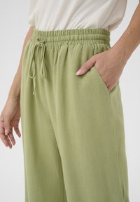 Ljust gröna, texturerade, löst sittande byxor med elastisk midja och dragsko; har sidofickor och en avslappnad design.