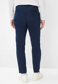 Navyblaue Baumwollmischungshosen mit slim fit, ausgestattet mit Gesäßtaschen und einer glatten Textur. Kombiniert mit weißen Sneakers.