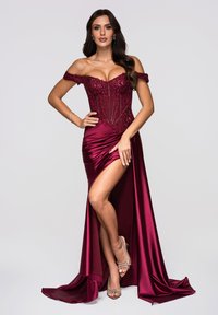Bordowa satynowa suknia z dekoltem odsłaniającym ramiona, koronkowym gorsetem ozdobionym koralikami i rozcięciem powyżej uda. Charakteryzuje się gładką fakturą i eleganckim układem materiału.