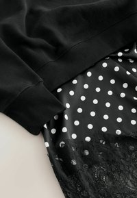 Black sweatshirt with ribbed cuffs joins a black polka dot satin skirt, featuring a lace trim at the hem. Smooth texture and layered design.