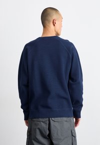 Donkerblauwe textuur sweatshirt met een ronde hals en geribbelde manchetten, met een relaxte pasvorm en raglanmouwen, gedragen met grijze cargobroeken.