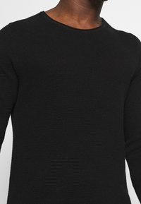 Schwarzer Strickpullover mit Rundhalsausschnitt, der ein strukturiertes Muster und lange Ärmel aufweist, entworfen für eine taillierte Silhouette.
