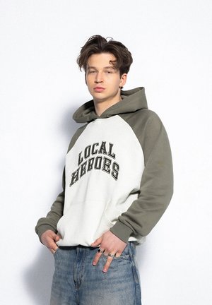 Bluza z kapturem z białym przodem i oliwkowymi rękawami, z napisem "LOCAL HEROES", przednią kieszenią i luźnym krojem.