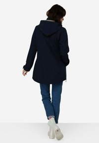 Chaqueta impermeable navy con capucha, de diseño de longitud media y cierre con cremallera. Combinada con jeans de color azul claro y calzado blanco brillante.