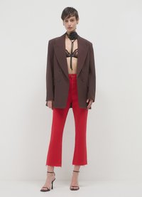 Brauner zweireihiger Blazer über einem schwarzen Spitzen-BH, kombiniert mit hoch taillierten, roten verkürzten Jeans und schwarzen Riemchen-Pumps.