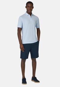 Camisa polo de color azul claro con mangas cortas, combinada con pantalones cortos azul marino. Modelo con zapatillas de deporte azul oscuro. Diseño sencillo, tejido transpirable.