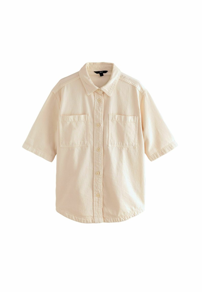 Chemise à manches courtes beige clair, avec un col, deux poches poitrine et une coupe décontractée. Le tissu semble doux et légèrement texturé.
