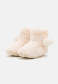 Fuzzy pink plush slippers with a rounded toe, cuffed top, and a pom-pom detail on the side. Soft texture with a beige sole.