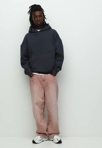 Marineblå hoodie med løs pasform, parret med lyse rosa denimjeans. Outfitten inkluderer hvide sneakers med sorte detaljer.