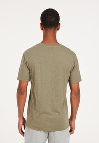 Camiseta de manga corta verde oliva con cuello redondo, fabricada en un tejido ligero y con un corte relajado. Presenta un dobladillo recto y un diseño minimalista.