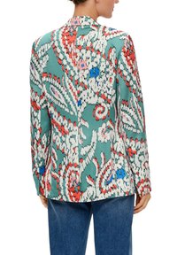 Bunter Blazer mit Blumenmuster in hellem Teal, mit seidig glatter Textur, Reverskragen und langen Ärmeln, kombiniert mit dunklen Jeans.