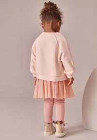 Sweat-shirt rose clair avec une finition texturée et duveteuse, jupe en tulle superposée, leggings côtelés rose clair et baskets montantes décoratives pastel.