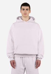 Sweatshirt à capuche rose clair en tissu doux. Comprend une poche kangourou à l'avant, des poignets côtelés et un petit logo sur la poitrine.