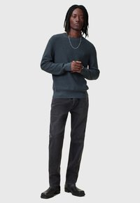 Maglione a maglia grigio scuro con polsini a coste, abbinato a jeans neri a gamba dritta e stivaletti neri. Collana semplice in argento.