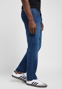 Modre jeans hlače ravnega kroja, z petimi žepi in kontrastnim šivanjem, v kompletu z belimi športnimi čevlji s črnimi črtami.